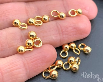 May include: Gold-toned metal bead chain connectors with a loop on one end and two beads on the other. The connectors are shown on a hand.