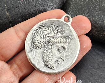 May include: Silver pendant featuring a detailed profile of a man with a beard and a crown. The pendant is round and has a loop at the top for attaching a chain.