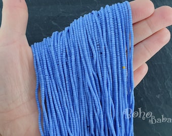 May include: A close-up of a hand holding a bundle of light blue glass seed beads. The beads are small and uniform in size, and they are arranged in a neat, even row.