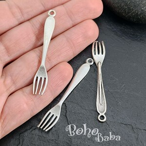 Op de afbeelding: Drie zilverkleurige vorkcharms met een lus aan de bovenkant om aan sieraden of andere knutselwerkjes te bevestigen. De vorken zijn ongeveer 5 cm lang.