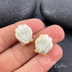 以下が含まれることがあります： 白とベージュの貝殻の形をしたイヤリングのペア。イヤリングは骨を彫って作られており、自然で有機的な外観をしています。