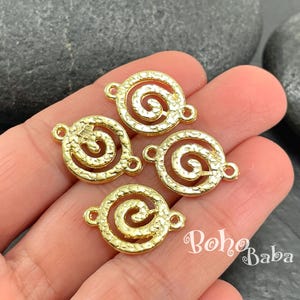 Puede incluir: Cuatro colgantes dorados en forma de espiral, con superficies texturizadas y pequeños bucles para sujetar a la joyería. Los colgantes son redondos con un diseño en espiral en el centro. Los colgantes se sostienen en una mano.