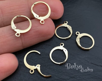 May include: Five gold-toned earring hoops with a hinged closure. The hoops are arranged on a hand and a dark surface.