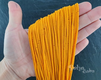 May include: A close-up of a hand holding a bundle of bright orange seed beads. The beads are small and uniform in size, creating a smooth, even texture.