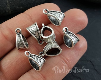 May include: A close-up of eight silver-toned pendant bails, each with a teardrop shape and a small loop at the top. The bails are arranged on a hand, with the loop facing up.