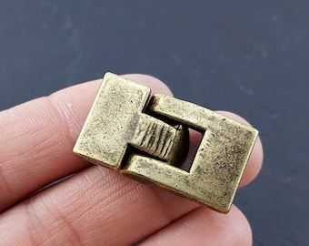 Könnte beinhalten: Ein goldfarbener Metallverschluss mit rechteckiger Form und einem Scharnier. Der Verschluss ist geschlossen und hat eine strukturierte Oberfläche.