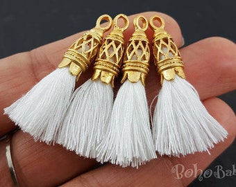 May include: Four white tassel charms with gold metal tops. The tops have a decorative, intricate design.