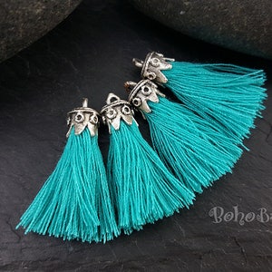 May include: Four turquoise blue tassels with silver metal tops. The tassels are arranged in a semi-circle on a dark gray surface.