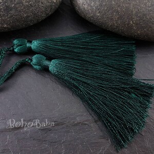 Puede incluir: Dos borlas de color verde oscuro con largas hebras de flecos. Las borlas están atadas juntas con un cordón verde oscuro.