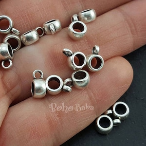 May include: Silver-toned metal jump rings with a round shape and a small loop on one side. The jump rings are used for connecting jewellery pieces.