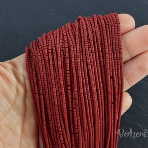 Könnte beinhalten: Nahaufnahme eines Bündels roter Perlen. Die Perlen sind klein und zylindrisch und in einer ordentlichen, gleichmäßigen Reihe angeordnet. Die Perlen haben eine tiefe, satte rote Farbe und eine leicht glänzende Oberfläche.