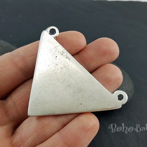 May include: A silver-toned, triangular jewellery component with two small loops at the top for attachment. The metal has a slightly distressed finish, giving it a vintage or handmade appearance. The Boho Baba logo is visible in the bottom right corner.