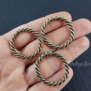 May include: Three gold-coloured metal rings with a twisted rope design. The rings are on a hand.