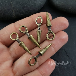 May include: Five antique gold-toned metal charms shaped like arrowheads with a loop at the top. The arrowheads are approximately 2.5 cm long.