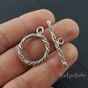 May include: Silver-toned metal toggle clasp with a rope-like design. The clasp has a round ring and a straight bar.