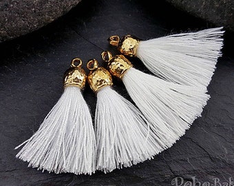 May include: Four white tassel charms with gold hammered metal tops.