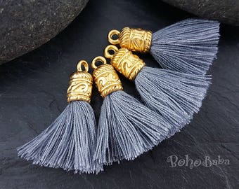 May include: Four gray tassel charms with gold metal caps. The caps have an ornate design.