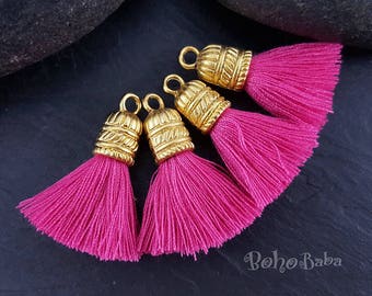 May include: Four pink tassel charms with gold metal caps. The tassels are made of soft, fluffy yarn and are perfect for adding a touch of bohemian style to your jewelry or crafts.