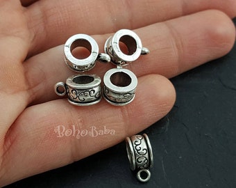 May include: Five silver metal bead caps with an ornate design. The bead caps have a hole in the center and a small loop on the side.