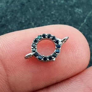 May include: A silver-toned ring with a circle of black gemstones. The ring has a small loop on each side for attaching to a chain or other jewelry.
