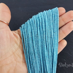 May include: A close-up of a hand holding a strand of light blue seed beads. The beads are small and uniform in size, and they are arranged in a neat, straight line. The beads are perfect for jewelry making, beading projects, and crafting.