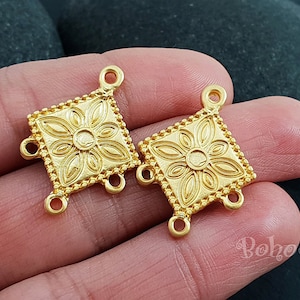 May include: Two gold-tone metal connector charms with a square shape and a floral design. Each charm has four jump rings.