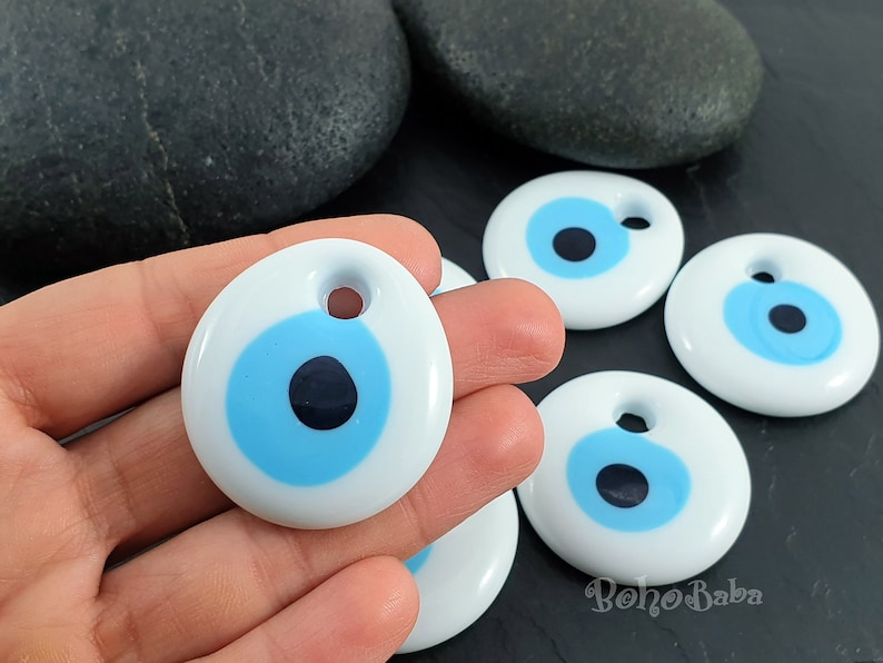 May include: Five white ceramic evil eye charms with blue and black eyes. The charms have a hole at the top for hanging.