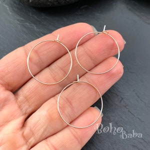 May include: Three delicate, rose gold-coloured hoop earring findings. Each hoop is circular with a small loop at the top for attaching to an ear wire. The hoops are displayed against a dark background.
