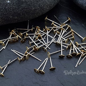 Puede incluir: Un mont&oacute;n de postes de pendientes de color dorado con tallos plateados. Los postes est&aacute;n esparcidos sobre una superficie gris oscura.