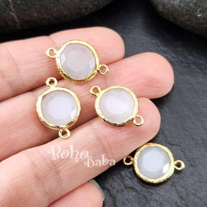 Pode incluir: Quatro pingentes de metal dourado com inserções de pedra opaca branca. Cada pingente tem dois anéis de salto para prender em joias.