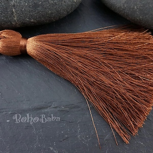 May include: A brown tassel with a long, flowing fringe. The tassel is made of soft, silky fibers and has a simple, elegant design.