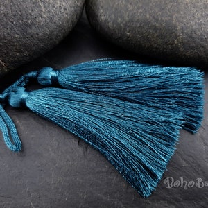 Op de afbeelding: Twee teal blauwe kwastjes met een lang koord. De kwastjes zijn gemaakt van zachte, zijdeachtige draden en zijn perfect om een ​​toets van elegantie aan elk project toe te voegen.
