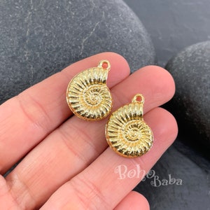 Op de afbeelding: Twee goudkleurige metalen bedels in de vorm van nautilus schelpen. De bedels hebben een gedetailleerd, getextureerd oppervlak en een lus aan de bovenkant om te bevestigen aan sieraden of andere knutselwerkjes.
