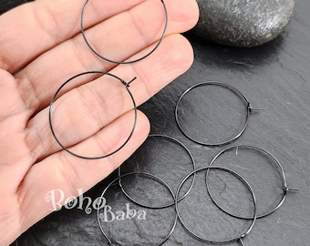 May include: Six black hoop earrings, each with a simple circular design. The earrings are displayed on a hand and a dark surface.