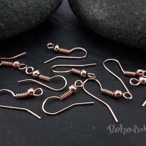 May include: Rose gold earring hooks with a spring and a small ball at the top. The hooks are scattered on a dark grey surface.