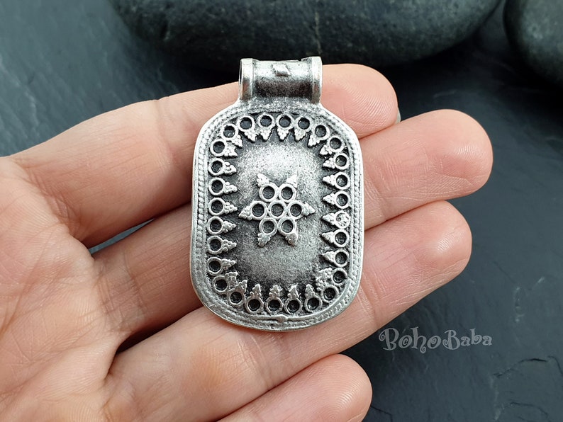 May include: Silver pendant with a star design and a decorative border. The pendant has a loop at the top for attaching a chain.