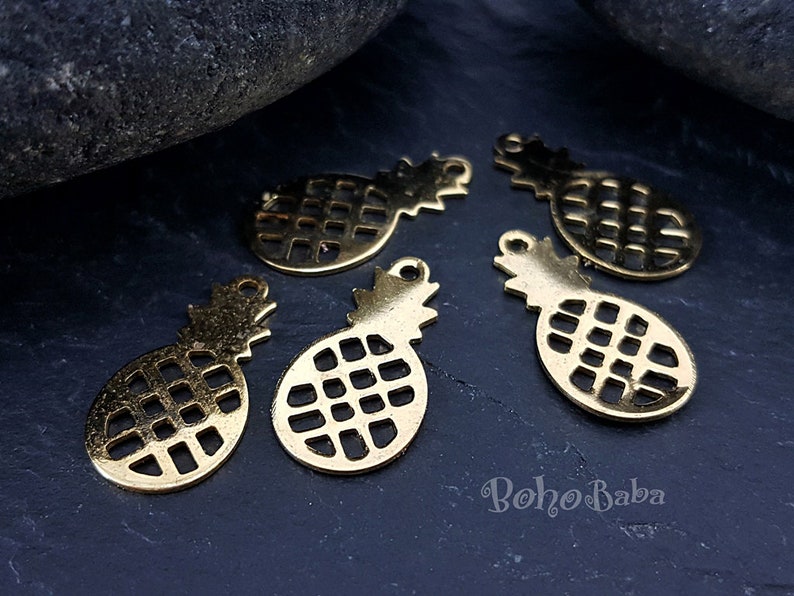 May include: Five gold-coloured metal pineapple charms with a cutout design. The charms have a loop at the top for attaching to jewellery or other crafts.