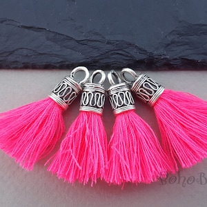 May include: Four pink tassel charms with silver metal tops. The tassels are made of soft, fluffy yarn and the tops have an intricate design.