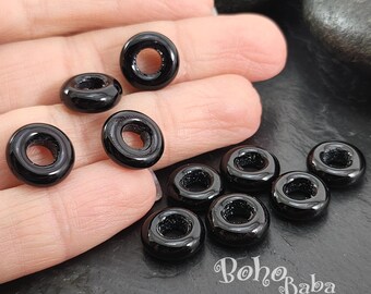 May include: Ten black donut-shaped beads with a hole in the center. The beads are arranged in a semi-circle on a hand.