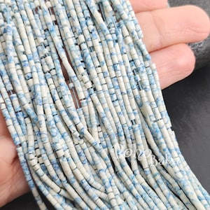 Puede incluir: Una hebra de cuentas de cerámica blanca y azul. Las cuentas son pequeñas y cilíndricas, con un patrón de mármol. Las cuentas están enhebradas en un alambre delgado.