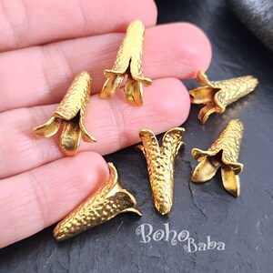 Puede incluir: Seis tapones de cuentas de metal dorado en forma de flor con una superficie texturizada. Los tapones de cuentas miden aproximadamente 2,5 cm de largo.