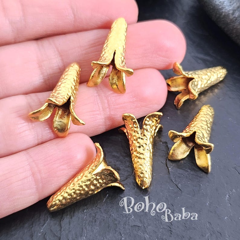 Puede incluir: Seis tapones de cuentas de metal dorado en forma de flor con una superficie texturizada. Los tapones de cuentas miden aproximadamente 2,5 cm de largo.