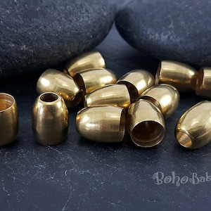 May include: A group of 13 gold-coloured metal beads, each with a cylindrical shape and a smooth, polished finish. The beads are scattered on a dark grey surface.
