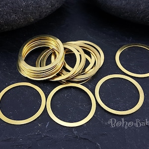 May include: A pile of gold-coloured metal rings, some stacked and some spread out on a black surface. The rings are all the same size and have a smooth, polished finish.