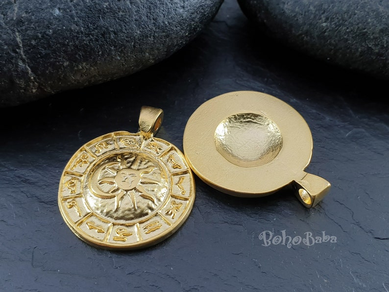 May include: Gold-toned pendant featuring a circular design with zodiac symbols and a sun and moon graphic. The back of the pendant is plain.