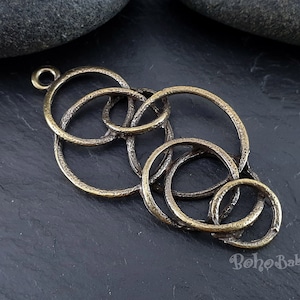 May include: A gold-toned metal pendant featuring an intricate design of overlapping circles. The pendant has a loop at the top for attaching to a chain or cord.