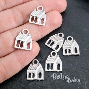 May include: Six silver charm pendants shaped like houses with a small loop at the top for attaching to a chain or bracelet. The charms are on a black surface.