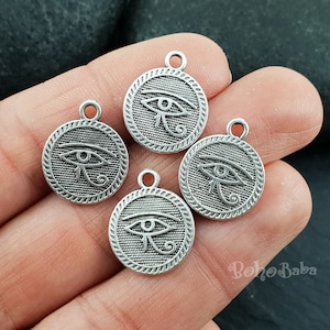May include: Four silver charm pendants with an Egyptian eye of Horus design. Each pendant has a circular shape with a raised edge and a detailed engraving of the eye of Horus symbol.