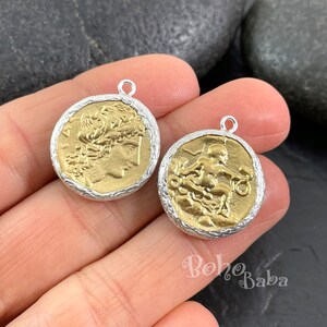 May include: Two gold-toned metal coin pendants with a silver-toned border. One pendant features a profile of a woman with a crown, the other features a figure of a person holding a scale.