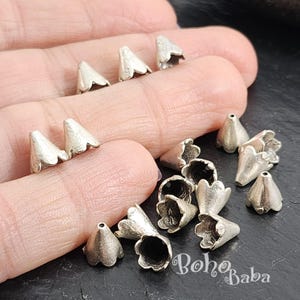 May include: Silver metal cone shaped bead caps with scalloped edges. The bead caps are arranged in a pile on a hand.